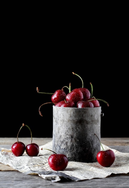 Cerises à l'intérieur d'une tasse en étain vintage avec de vieux journaux en dessous