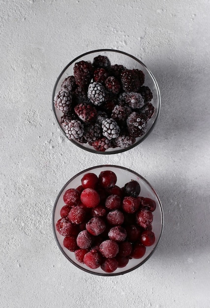 Cerises et mûres congelées dans deux bols transparents en verre sur fond de béton gris. Vue d'en-haut. Format vertical