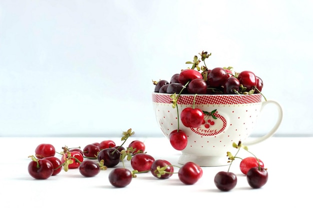 Cerises mûres dans une tasse et sur une table sur un fond blanc