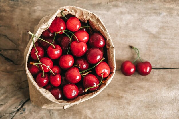 Cerises mûres fraîches dans un sac en papier sur fond de bois Vue de dessus Copier l'espace vide pour le texte