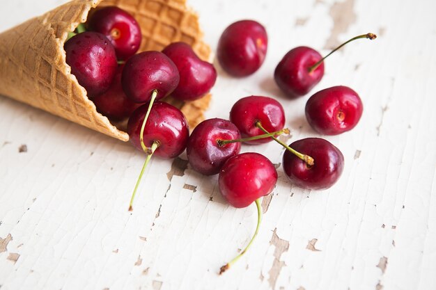 Les cerises mûres juteuses dans une tasse de gaufre se trouvent sur une vieille table blanche en bois