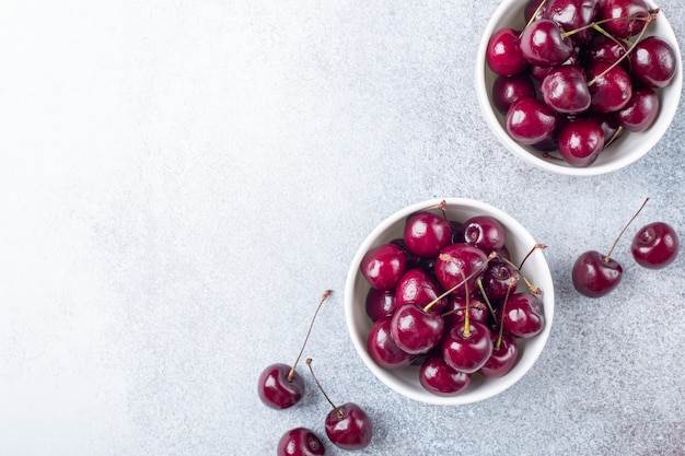 Cerises rouges mûres fraîches dans un bol blanc sur une pierre grise