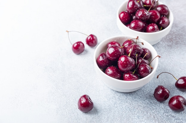 Cerises rouges mûres fraîches dans un bol blanc sur une pierre grise