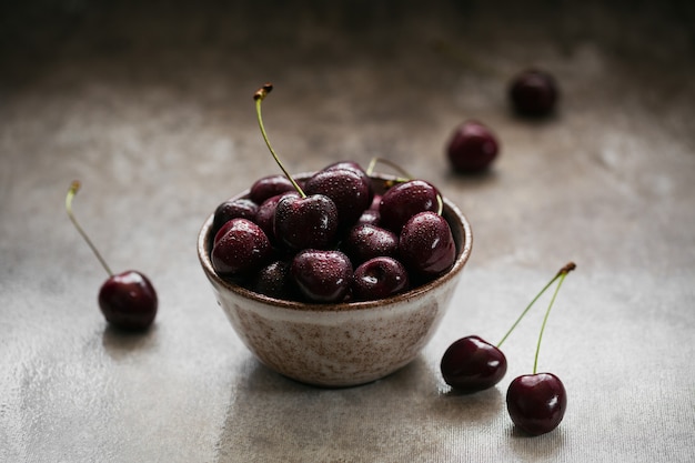 Cerises sucrées juteuses mûres avec des gouttes d'eau dans un bol en céramique sur fond sombre