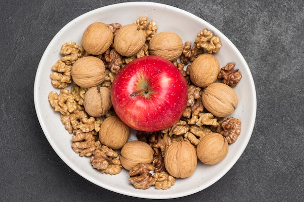 Cerneaux de noix, noix entières et pomme rouge dans un bol en céramique blanche