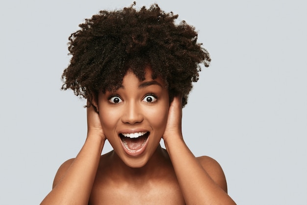 Certainement pas! Surpris jeune femme africaine regardant la caméra et souriant en se tenant debout sur fond gris