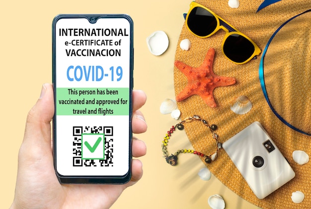 Certificat de vaccination contre le coronavirus ou passeport de vaccin pour le concept de voyageurs. Passeport électronique d'immunité COVID-19 dans l'application mobile pour smartphone pour les voyages internationaux. Fond de plage jaune avec chapeau