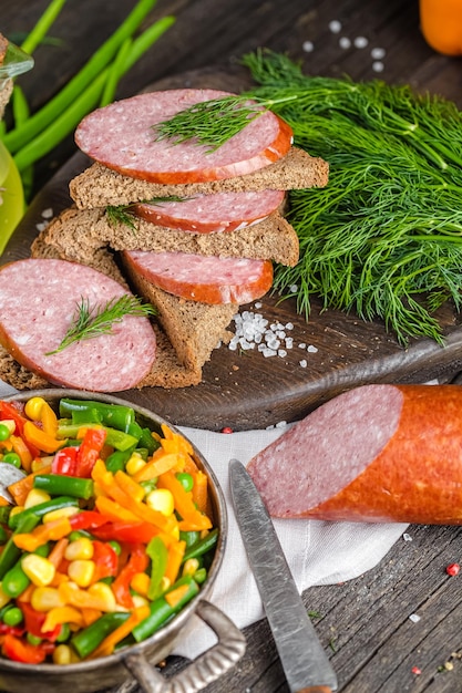 cervelat de saucisse ou salami, entier et en tranches, se trouve sur une table ou un arrière-plan rustique en bois, coupant