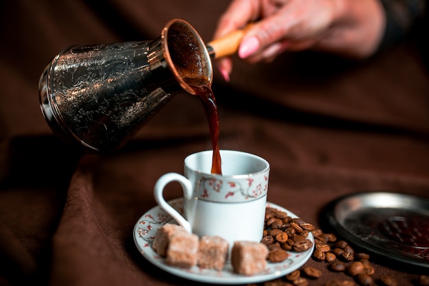 Cezve argenté et grains de café sur le textile marron foncé.