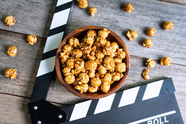 CFlat laïc de savoureux pop-corn au caramel et clap sur une table en bois, vue de dessus. Concept de temps de film