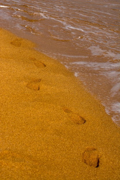 Une chaîne d&#39;empreintes nues dans le sable. Vagues sur la côte, plage de sable. Mousse à l&#39;eau de mer.