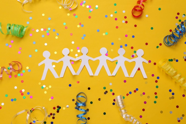 Chaîne de personnes coupées en papier avec des banderoles colorées et des confettis sur fond jaune Célébrant l'unité