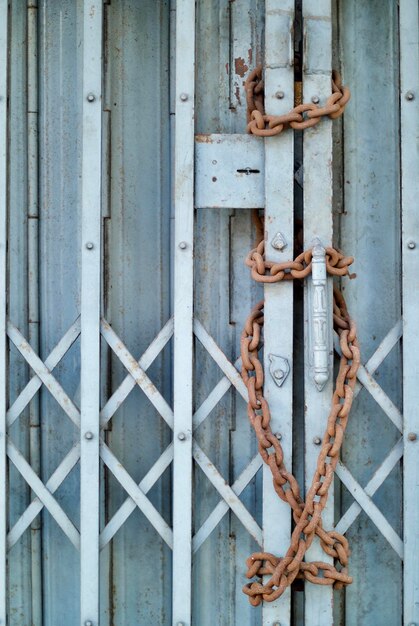 Une chaîne rouillée sur une porte métallique fermée par un mur bleu.