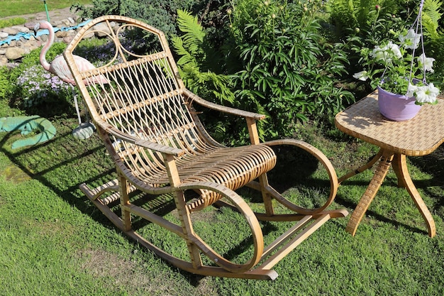 Chaise berçante pour les loisirs en rotin et petite table en osier dans le jardin d'été sur la pelouse en été