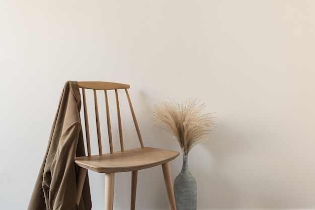 Chaise en bois avec chemise, herbe de la pampa dans un vase contre un mur blanc.