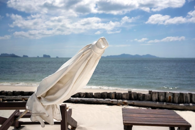 Chaise de plage vide avec le parapluie blanc avec du sable blanc et l'océan bleu en arrière-plan