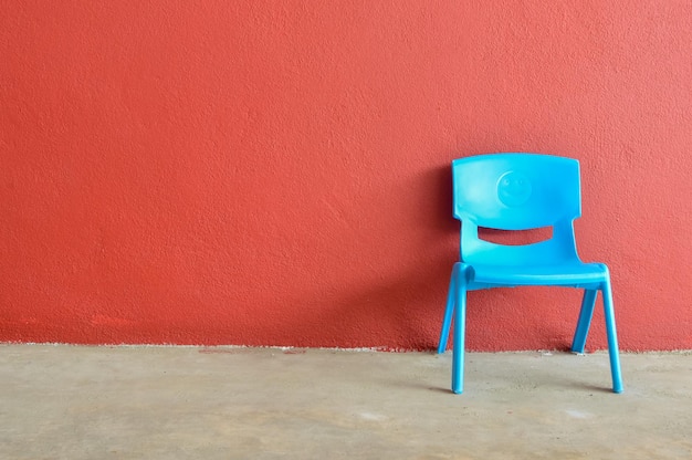 Chaise en plastique bleue posée contre le mur rouge Copiez l'espace pour le texte