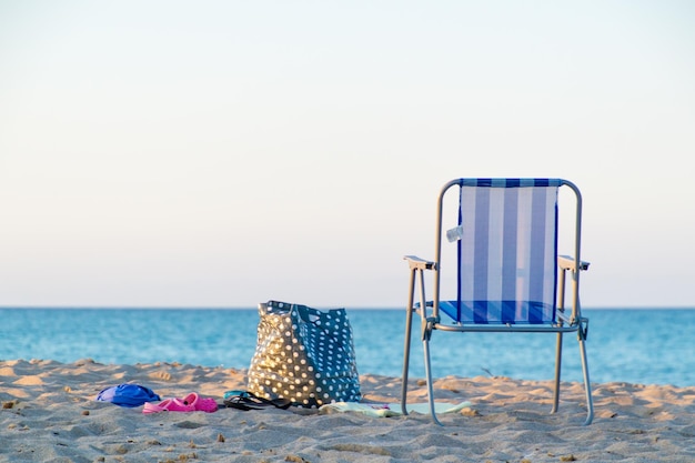 Une chaise pliant par sac sur le sable sur la plage contre un ciel dégagé