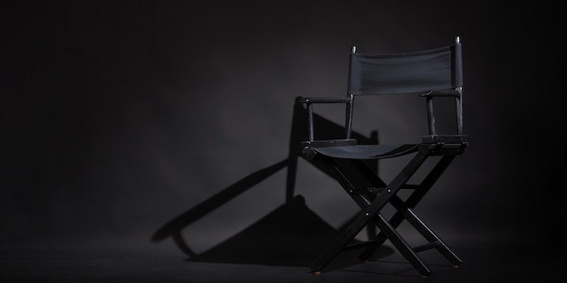 La chaise de réalisateur noire est isolée sur fond noir. Elle est utilisée dans la production vidéo ou l'industrie cinématographique. Prise de vue en studio.