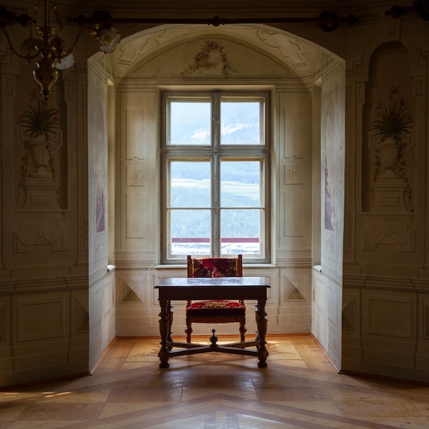 Une chaise et une table solitaires dans une vaste salle du château de Savoia, bâtiment de style architectural typiquement Walsen.