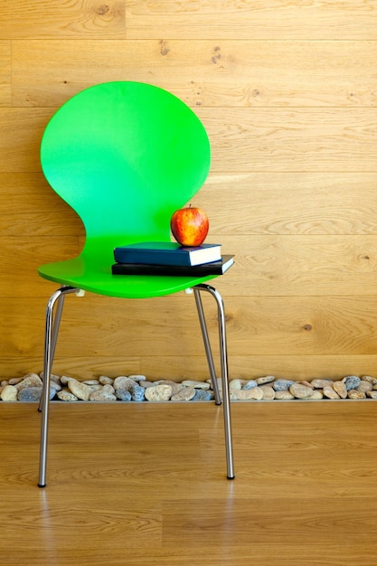 Chaise verte Pomme rouge et quelques livres contre un mur en bois Intérieur moderne