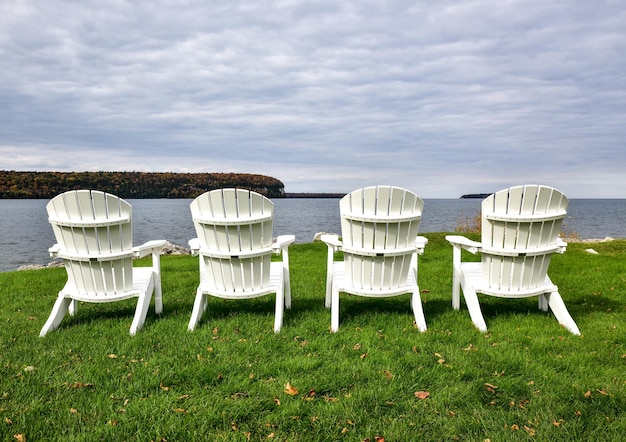 Des chaises adirondack vides au bord d'un lac herbeux contre un ciel nuageux