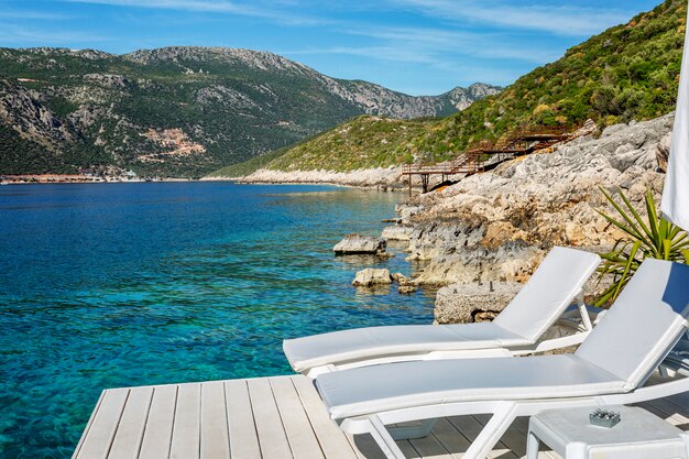 Chaises longues avec matelas beiges sur un plancher en bois au bord de la mer turquoise. Complexe de luxe. Beau paysage. Un repos serein. Tourisme et voyages.