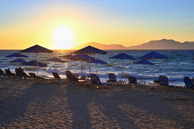 Chaises longues et parasol sur la plage au coucher du soleil au bord de la mer Beau concept pour les vacances d'été et les voyages