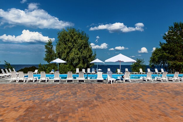 Chaises longues et parasols près de la piscine en bord de mer. Extérieur d'un complexe rural de vacances.