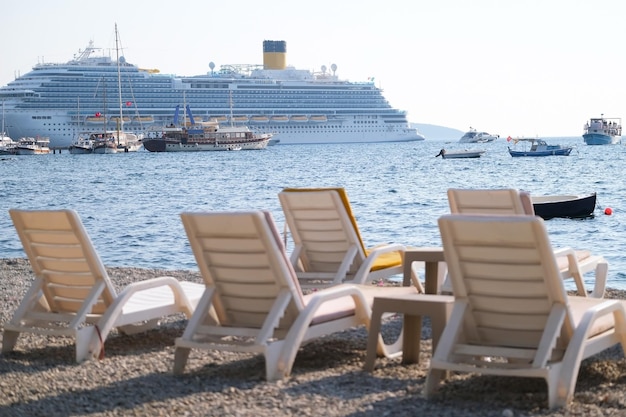 Des chaises longues se dressent sur la plage avec en toile de fond un grand paquebot