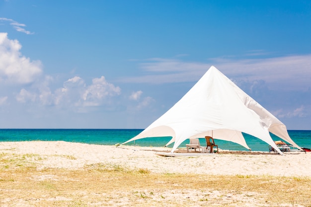 Les chaises longues sous le grand parasol sur la plage idyllique. tente blanche sur la plage.