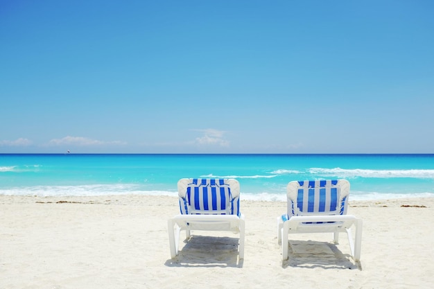 Des chaises de pont sur la plage contre un ciel bleu clair