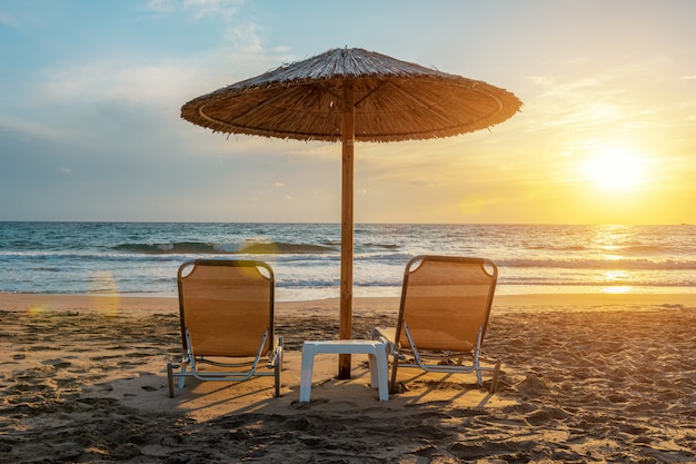 Chaises sous parasol sur la plage tropicale pendant le coucher du soleil