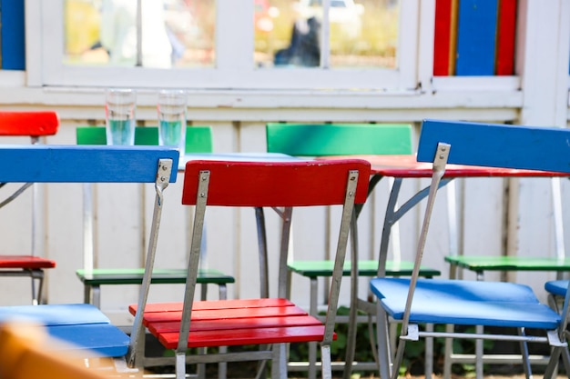 Des chaises vides et colorées disposées par table.