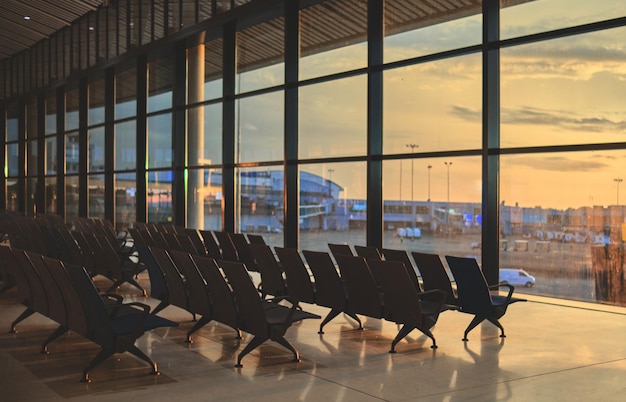 Chaises vides dans le hall de départ de l'aéroport avec vue sur le coucher du soleil Avion flou en arrière-plan