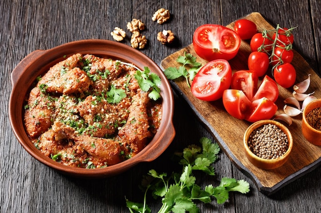 Chakhokhbili ragoût de poulet tomate aux herbes fraîches noix et épices dans un pot en argile sur une table en bois avec des ingrédients sur une planche à découper plat géorgien