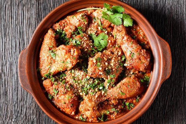 Chakhokhbili ragoût de poulet tomate avec des herbes fraîches, des noix et des épices dans un pot en argile sur une table en bois avec des ingrédients sur une planche à découper plat géorgien à plat