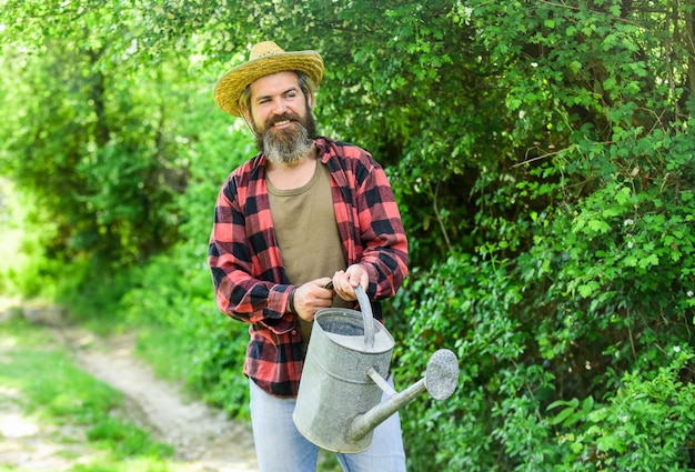 Chaleur d'été Équipement dans les mains des agriculteurs Style rustique Saturer le sol avec des nutriments L'homme tient un gros arrosoir Homme avec arrosoir dans le jardin Jardinage et arrosage des plantes Concept de jardinage