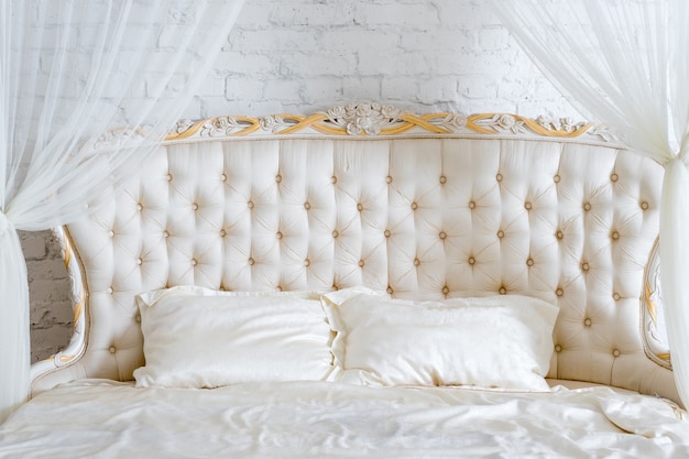 Photo chambre aux couleurs claires et douces. grand lit double confortable dans une élégante chambre classique. blanc élégant de luxe avec un design intérieur doré.