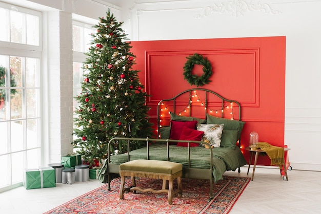 Une chambre décorée de Noël avec un arbre de Noël et une couronne sur le mur Un lit double dans un intérieur de Noël sur le fond d'un mur rouge