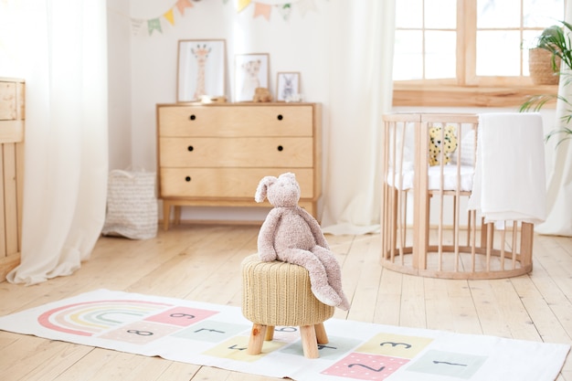 Photo chambre d'enfant scandinave: un panier à jouets, un lapin en peluche assis sur une chaise, un berceau pour un lit bébé. intérieur moderne d'une chambre d'enfant. rustique. copiez l'espace. hygge. intérieur de la maternelle