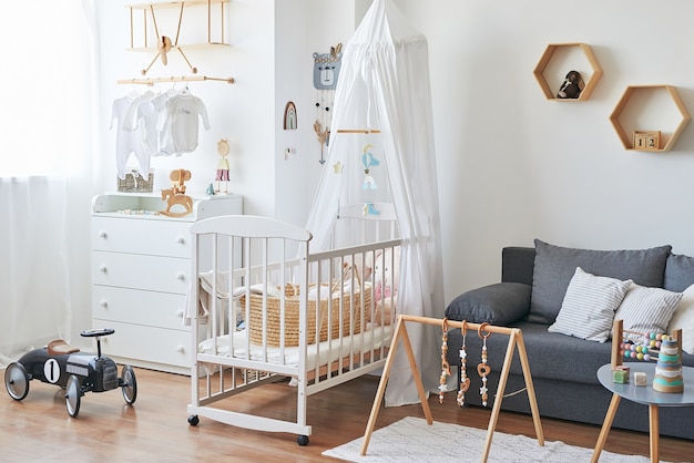 Chambre d'enfants intérieure blanche de style scandinave, chambre à coucher, pépinière. Lit bébé avec baldaquin. Étagères et jouets en bois. Simulateur de développement pour enfants.