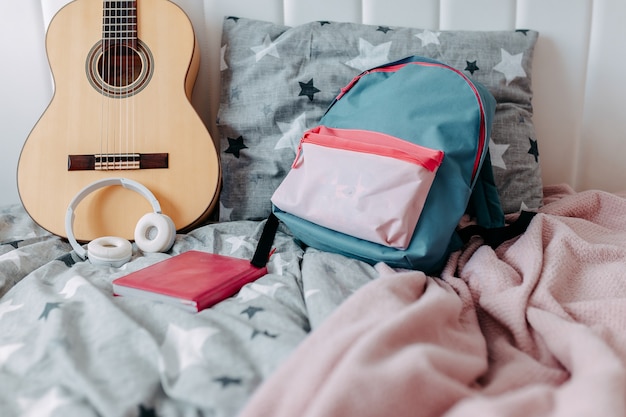 Chambre d'étudiant après étude. Guitare, sac à dos, écouteurs et ordinateur portable sur le lit.