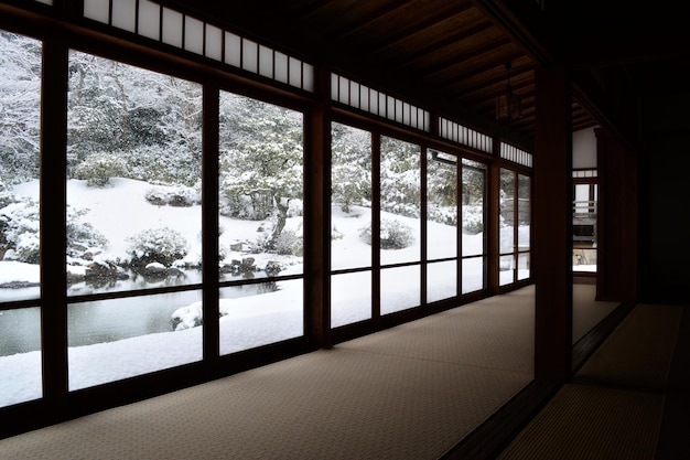 Chambre formelle de style japonais traditionnel avec vue sur le paysage d'hiver enneigé depuis les fenêtres panoramiques