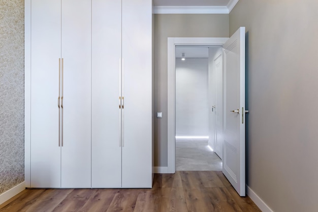 Chambre intérieure d'appartement blanc neutre avec porte de plancher en bois menant à une armoire coulissante de couloir et mur vide pour l'espace négatif Chambre vide de lumière naturelle
