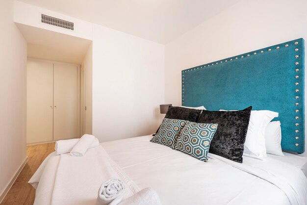 Chambre avec lit double avec tête de lit recouverte de tissu bleu avec rivets bleus, parquet clair et placard dans le couloir
