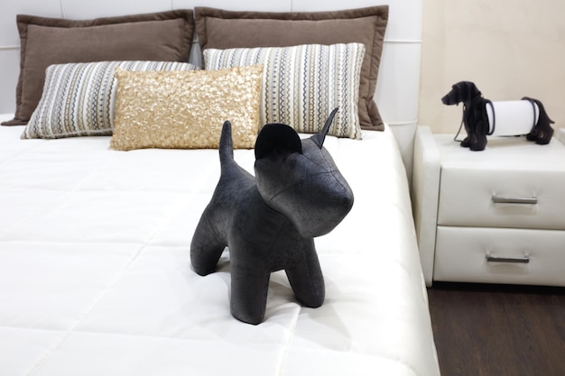 Chambre de luxe de style moderne avec jouet chien noir et différents oreillers sur lit blanc Intérieur d'une chambre d'hôtel