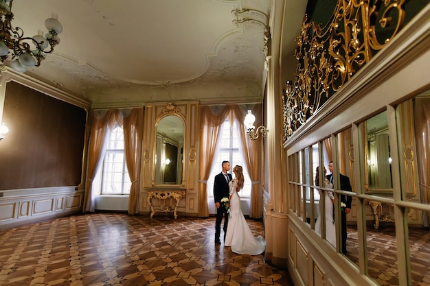 Chambre spacieuse avec de grandes fenêtres et de nombreux miroirs. les jeunes mariés se regardent. mariée tenant le bouquet de mariage.