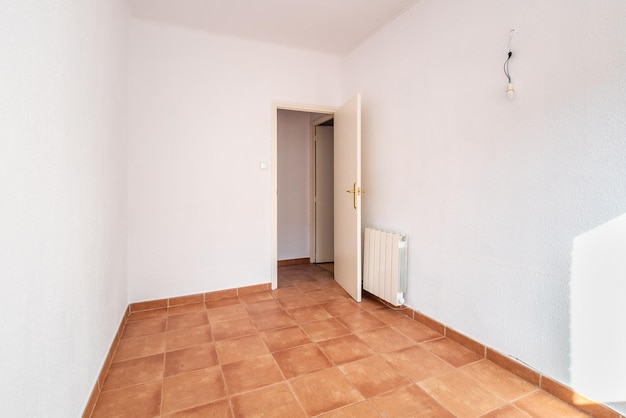 Une chambre spacieuse vide avec de vieux carreaux de sol carrés usés de couleur caramel et un radiateur au mur