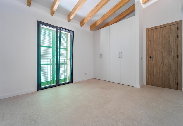 Chambre vide avec une fenêtre, des poutres en bois et des murs blancs